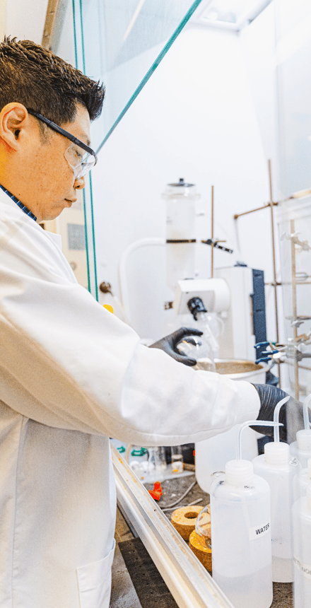 Scientist wearing safety glasses and lab coat conducting an experiment in a chemical laboratory.